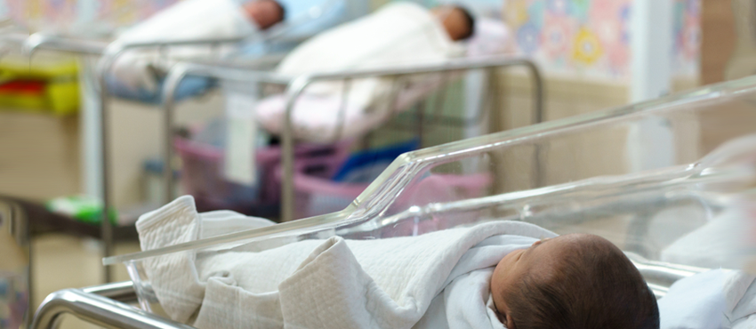 Photo showing newborn baby in hospital crib in foreground, with two more babies in the background.