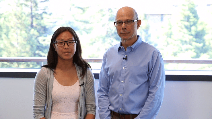 Moving gif image of an Asian female graduate student and a white male faculty member standing together at the Clark Center and speaking to the camera.