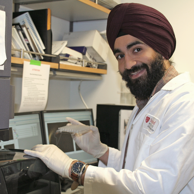 Photo of a male graduate student wearing a turban and working with laboratory equipment, holding up a sample.