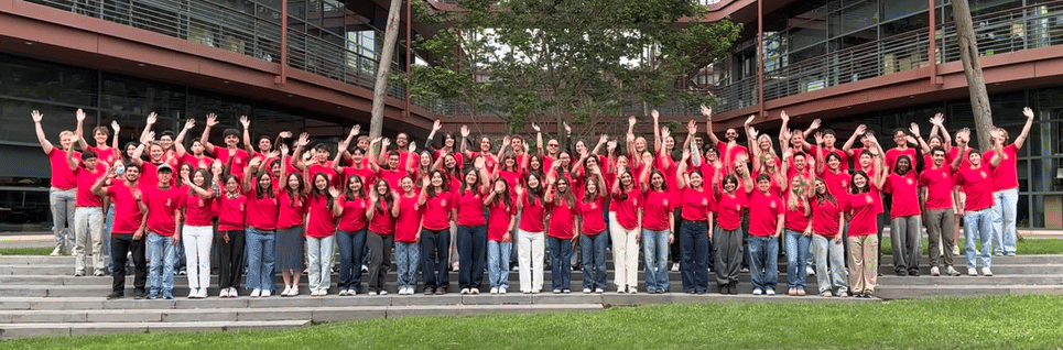 Animated gif of 70 undergraduate students outdoors at the Clark Center, wearing matching light red T-shirts and waving at the camera.
