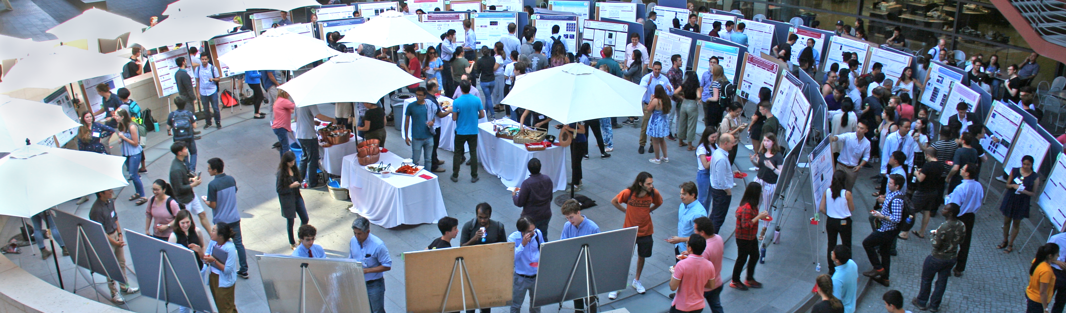 Photo taken from overhead of the Clark Courtyard, with dozens of posters and tables of food being visited by numerous people.