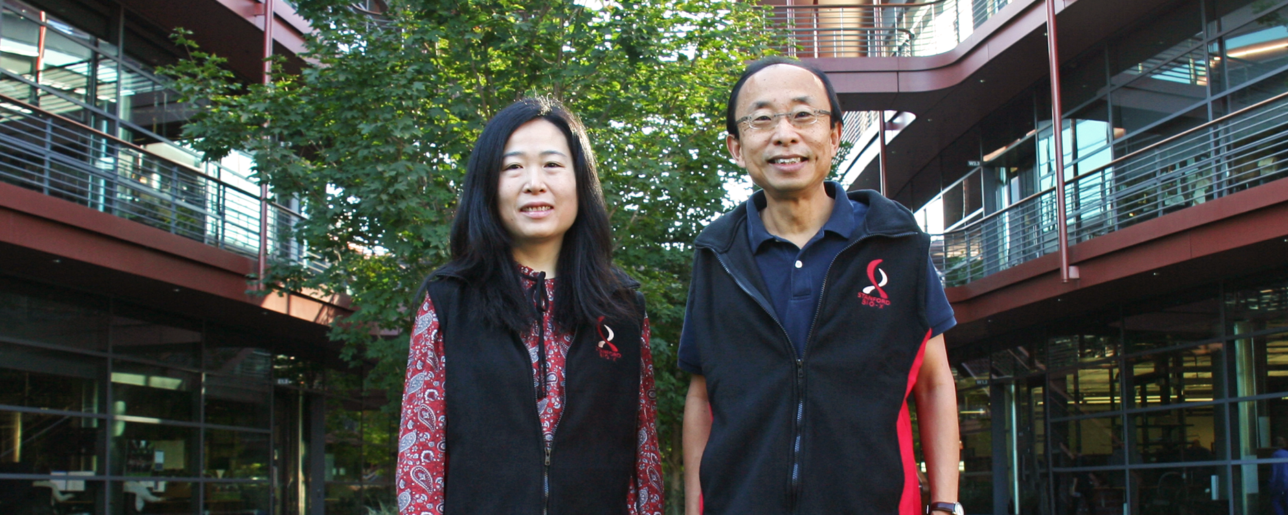 Photo of Drs. Ada Poon and H.-S. Phillip Wong standing in front of the Clark Center wearing fleece vests with the Bio-X logo. 