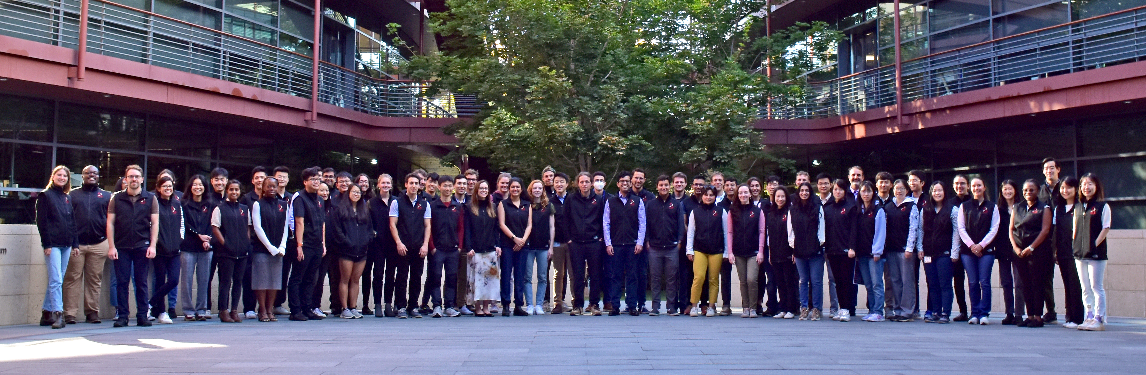 Outdoor group photo of graduate students wearing matching black vests.