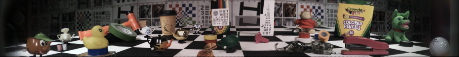 Very wide panorama of indoor space, with checkered floor upon which numerous random desktop/knickknack items are scattered.