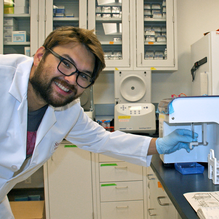 Photo of graduate student Alex Yoshikawa in the lab, using a flow cytometer machine.