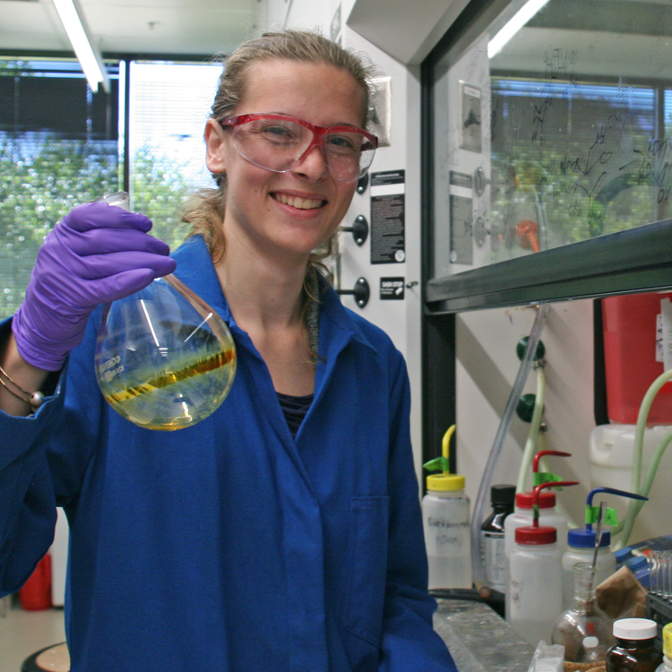 Photo of USRP student Ashley Utz in the laboratory, holding up a flask.