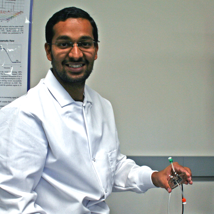 Photo of graduate student Ashwin Ramachandran in the lab, holding up a small electronic device.