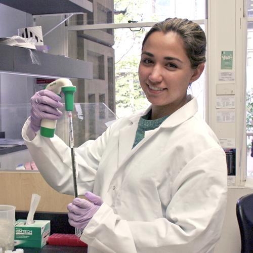 Photo of undergraduate student Avery Muniz in the laboratory, using a long pipette to extract a sample.