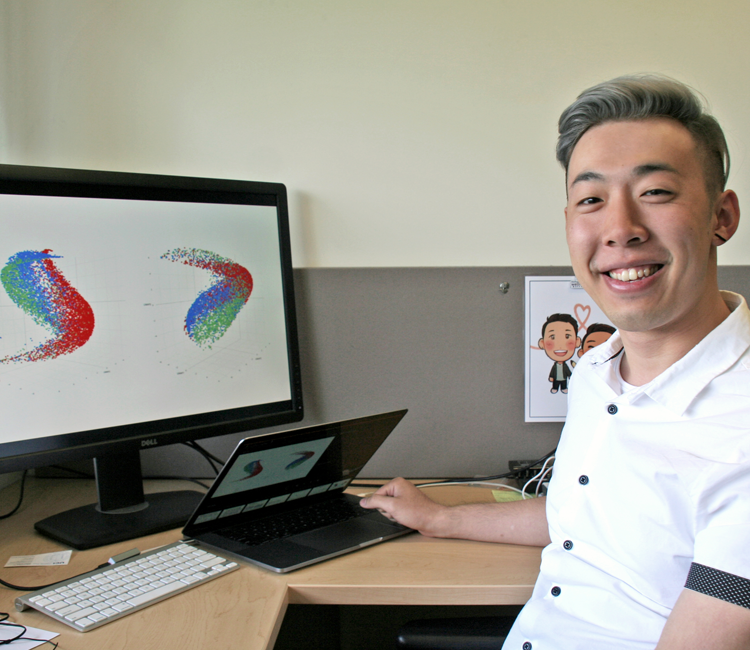 Photo of graduate student Lawrence Bai in a dry lab, working on a computer showing brightly-colored 3D images.