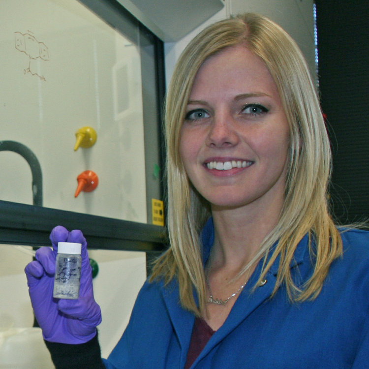 Photo of graduate student Caitlyn Miller in the lab, holding up a solution in a small vial.