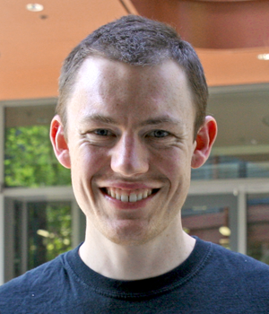 Outdoor headshot photo of smiling male graduate student with short dark hair.