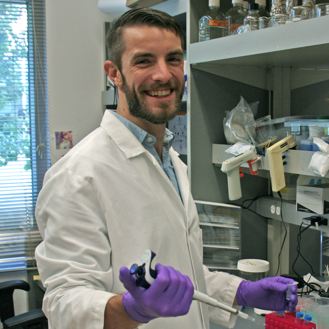Photo of graduate student David Glass in the lab, using a pipette at the bench.