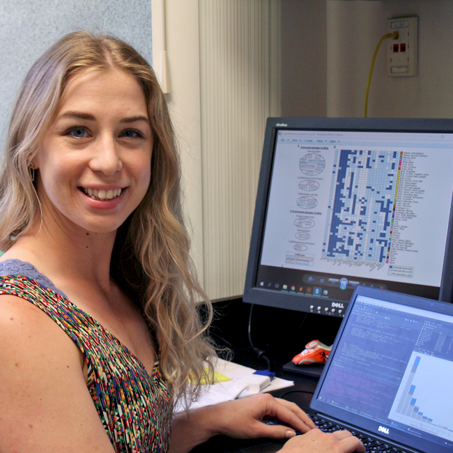 Photo of graduate student Olivia de Goede in a dry lab, working on a computer showing several colorful graphs.