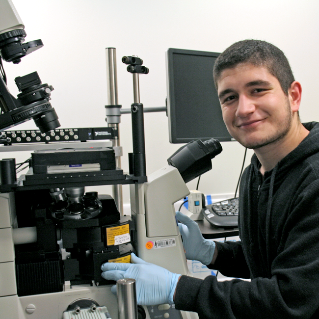 Photo of graduate student Elgin Korkmazhan in the lab, using a large microscope.