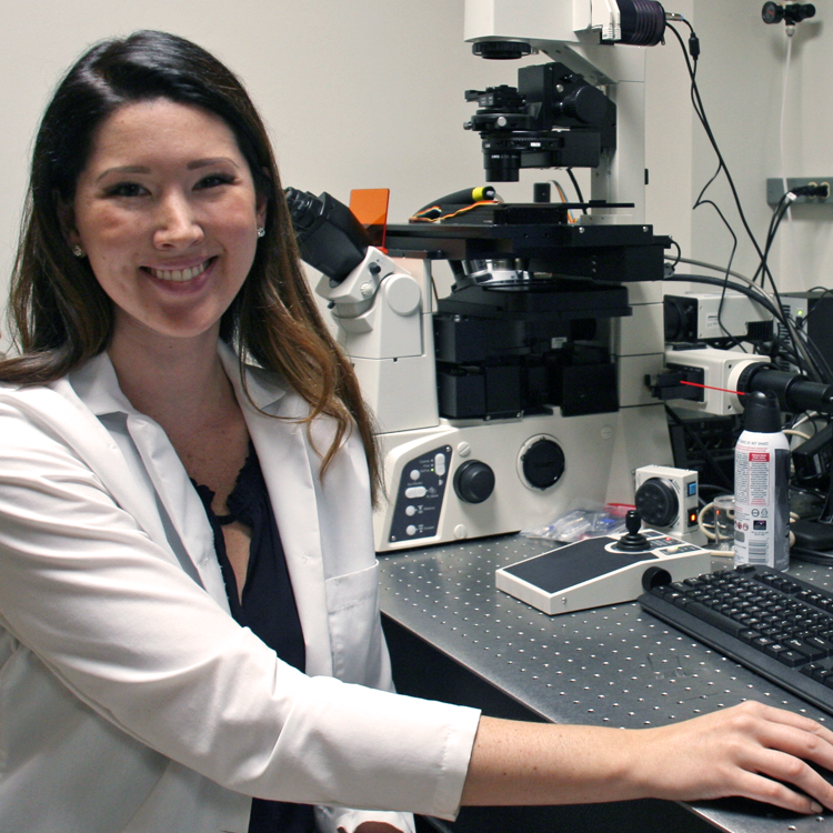 Photo of graduate student Eliza Adams in the lab, operating a computer and a microscope.