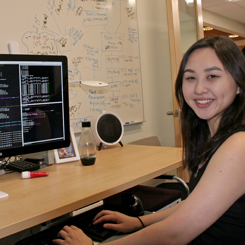 Photo of undergraduate student Emily Huang sitting in front of a computer monitor showing many lines of code.