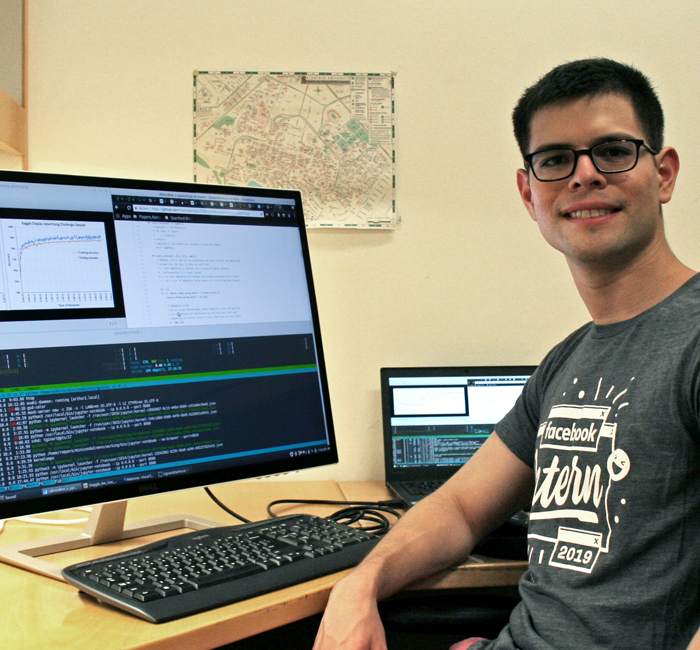 Photo of graduate student Tony Ginart in a dry lab, working on a computer with a large monitor showing computer code.