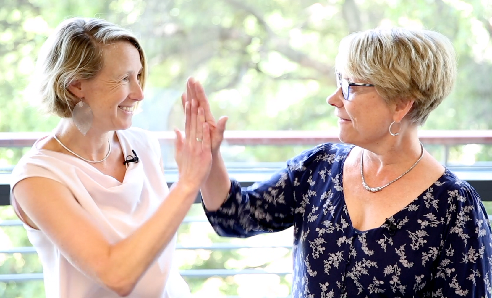 Two white female faculty members high-fiving in front of a window.