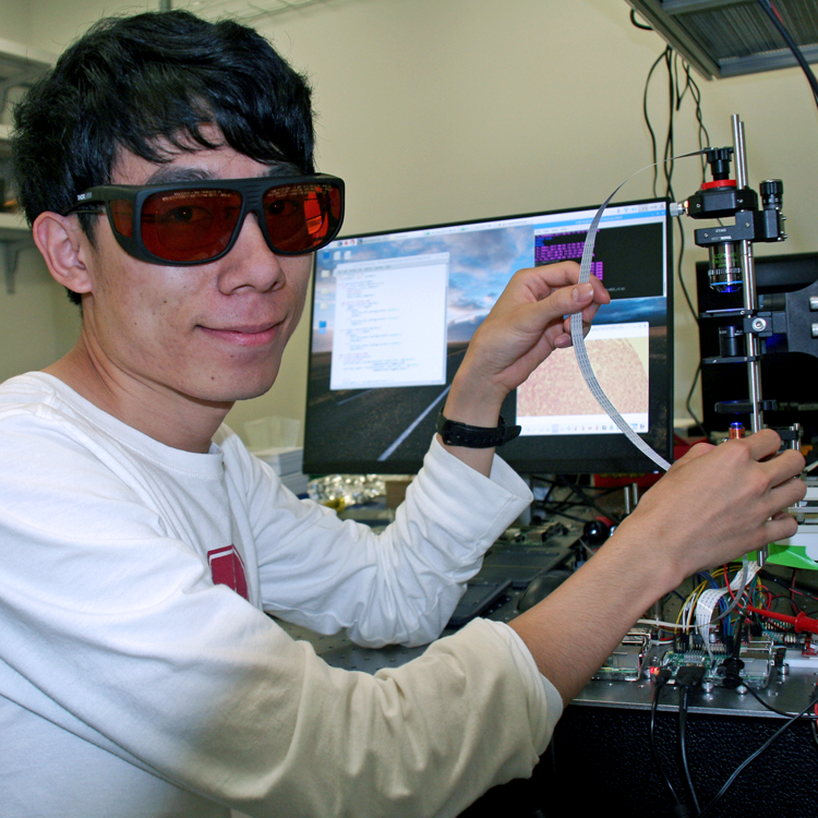 Photo of graduate student Hongquan Li in the lab, operating equipment while wearing red-tinted safety glasses.