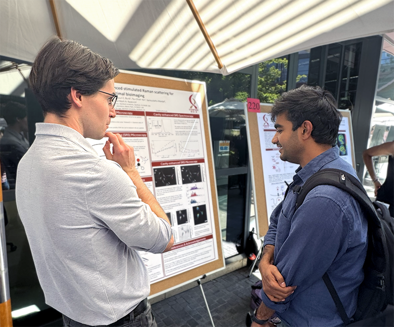 Outdoor photo of two young male researchers discussing a poster.