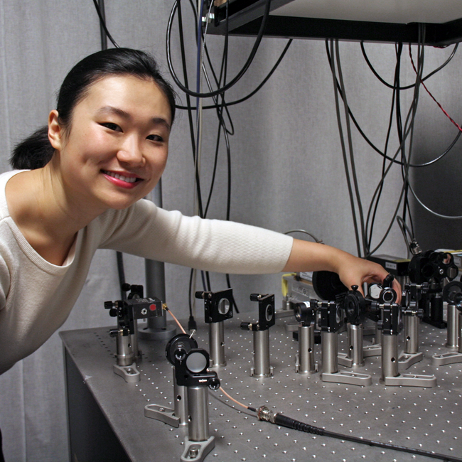 Photo of graduate student Jiarui Wang in the lab, leaning in towards a large silver laser setup.