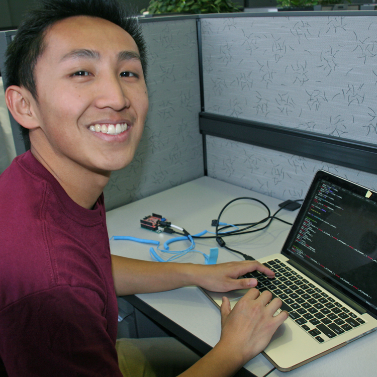 Photo of USRP student Jonathan Mak in the lab, working with a laptop computer hooked up to his monitoring device.