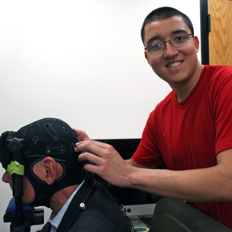 Photo of USRP student Jorge Delgado in the laboratory, having put a piece of monitoring headgear on Dr. Anthony Norcia.