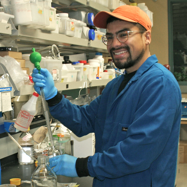 Photo of graduate student Jorge Meraz in the lab, working with a long, tube-shaped device.