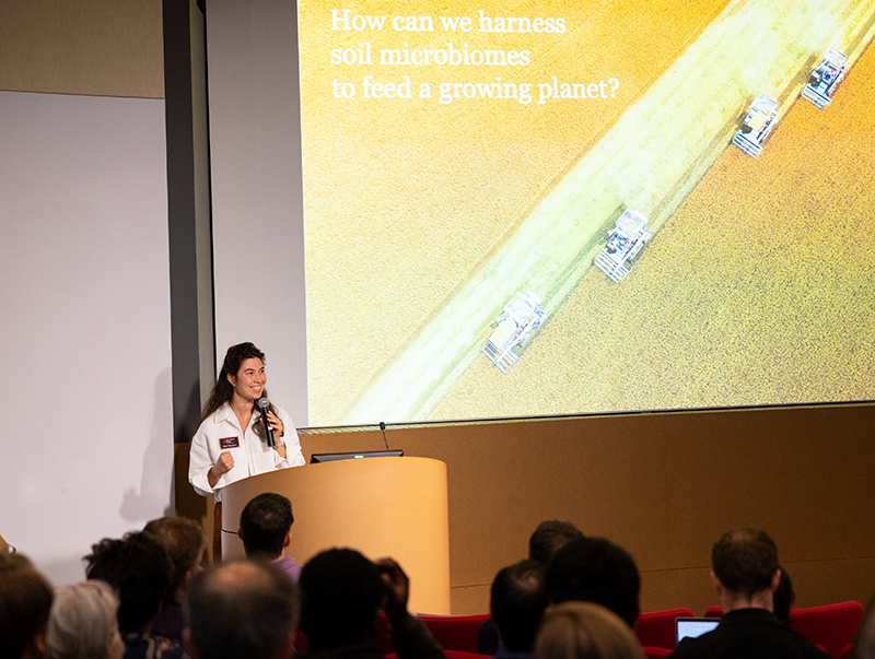 Indoor photo of a young female researcher presenting at the Clark Auditorium podium.