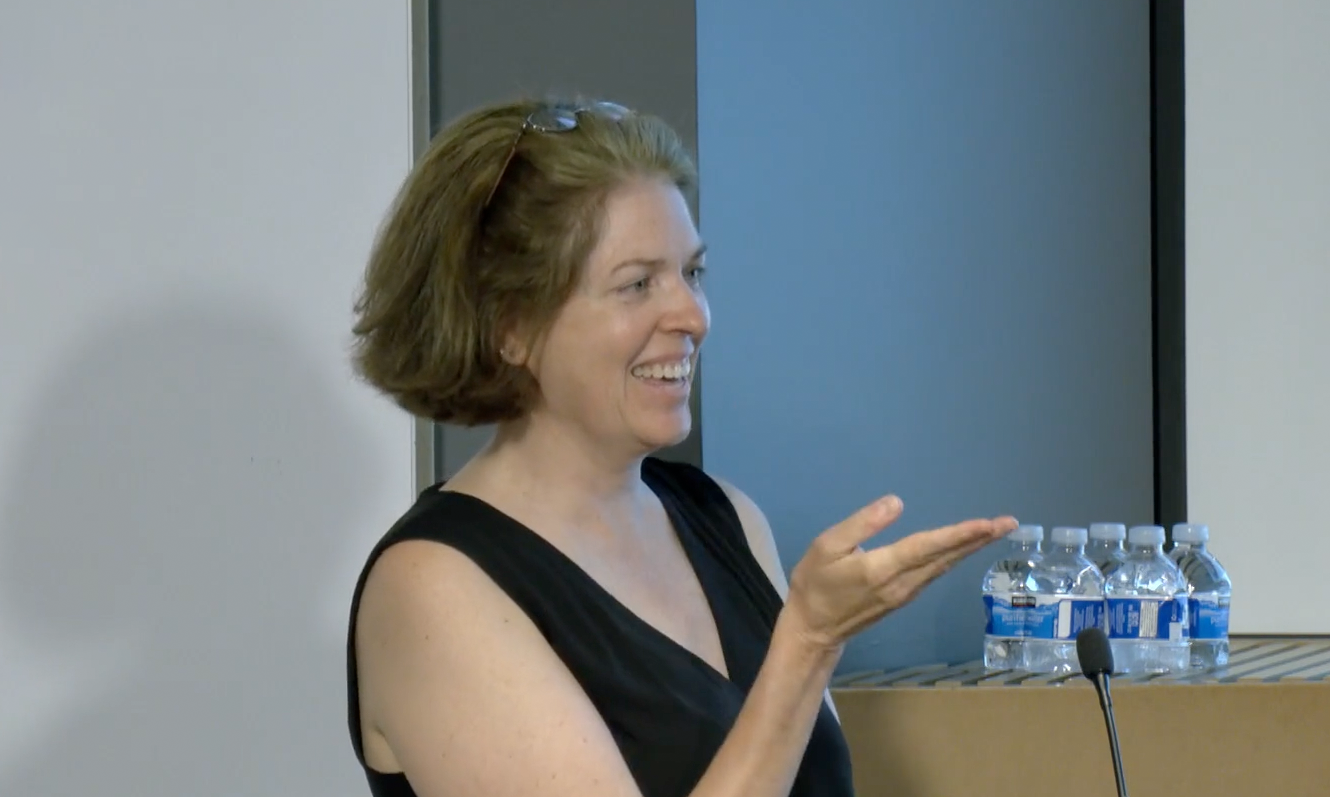 Indoor photo of white female faculty member speaking in front of a projector screen.