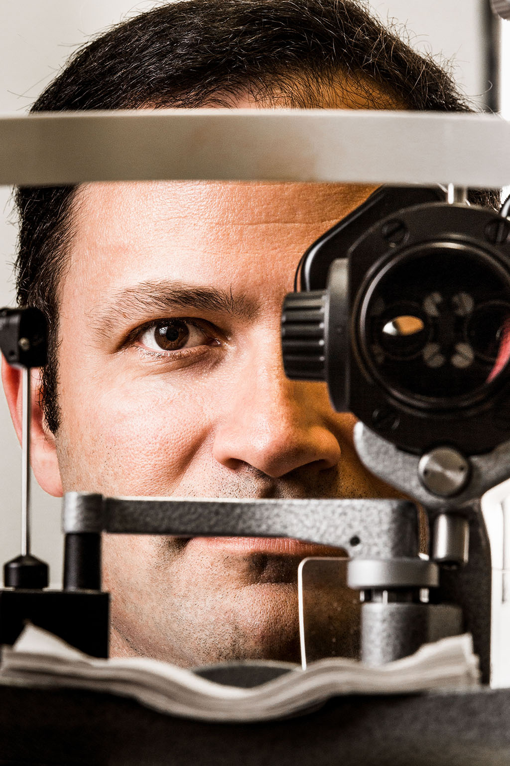Photo of man standing behind a vision assessment device, with one eye hidden by a lens and one showing.