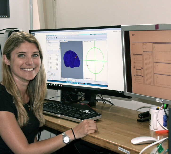 Photo of graduate student Molly Lucas in a dry lab, working on a computer showing a 3D model of a brain and many lines of code.