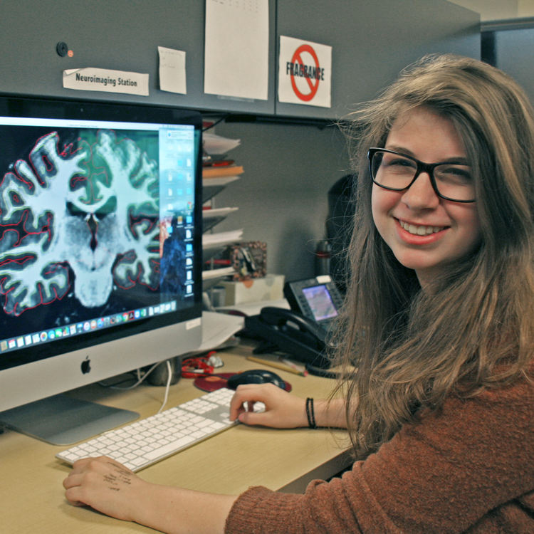Photo of USRP student Maggie Rosenthal in the laboratory, displaying a brain scan on a computer screen.