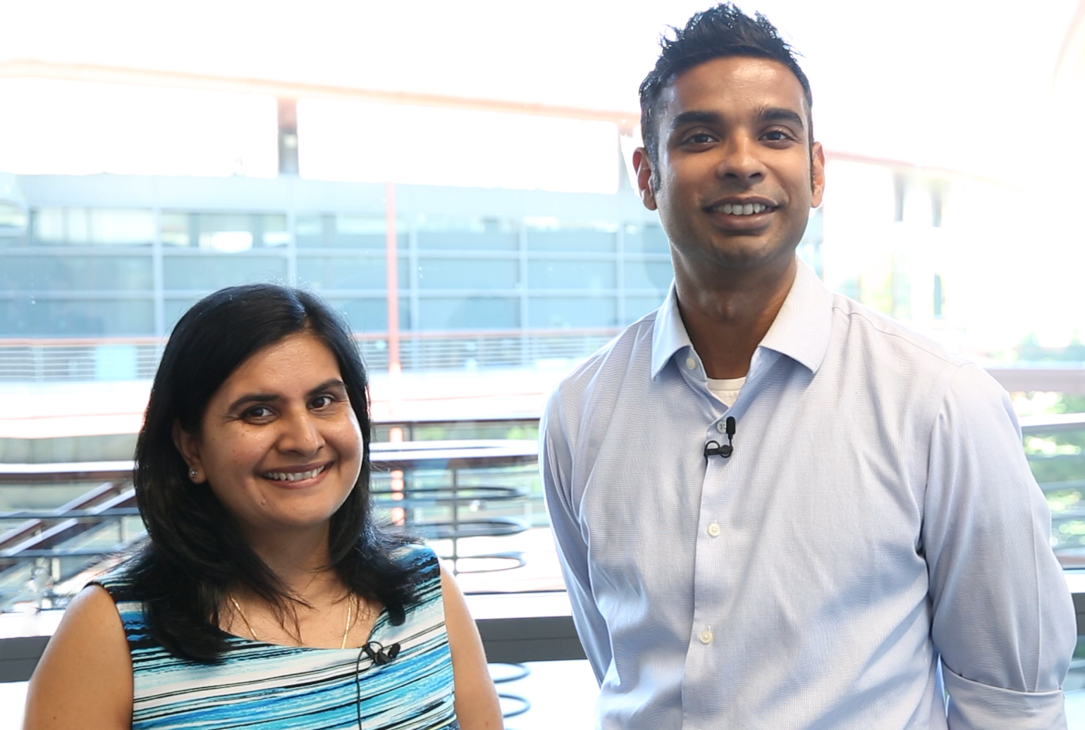 Indoor photo of two East Asian faculty members standing in front of a window, smiling at the camera.