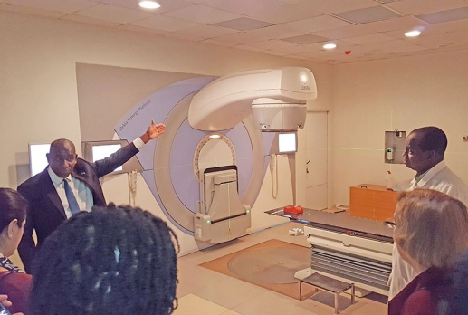 Photo of man in a suit gesturing to large piece of medical equipment in a hospital.