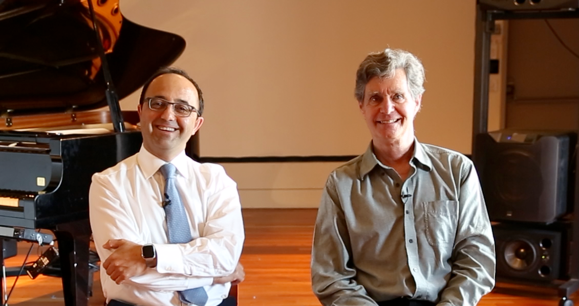 Indoor photo of two male faculty members seated in front of a grand piano.
