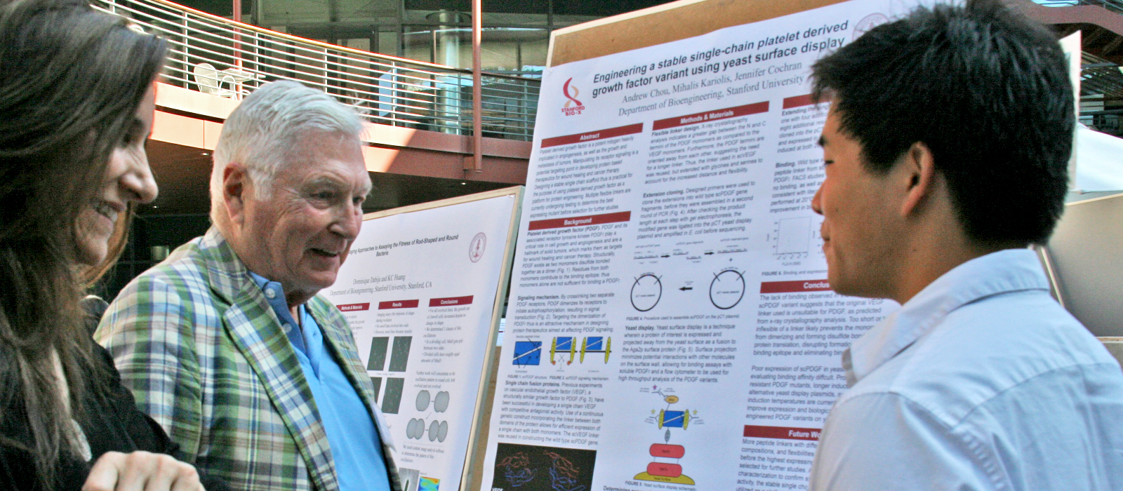 Photo of Pitch Johnson with a young student, standing at the student's scientific poster and smiling during discussion.