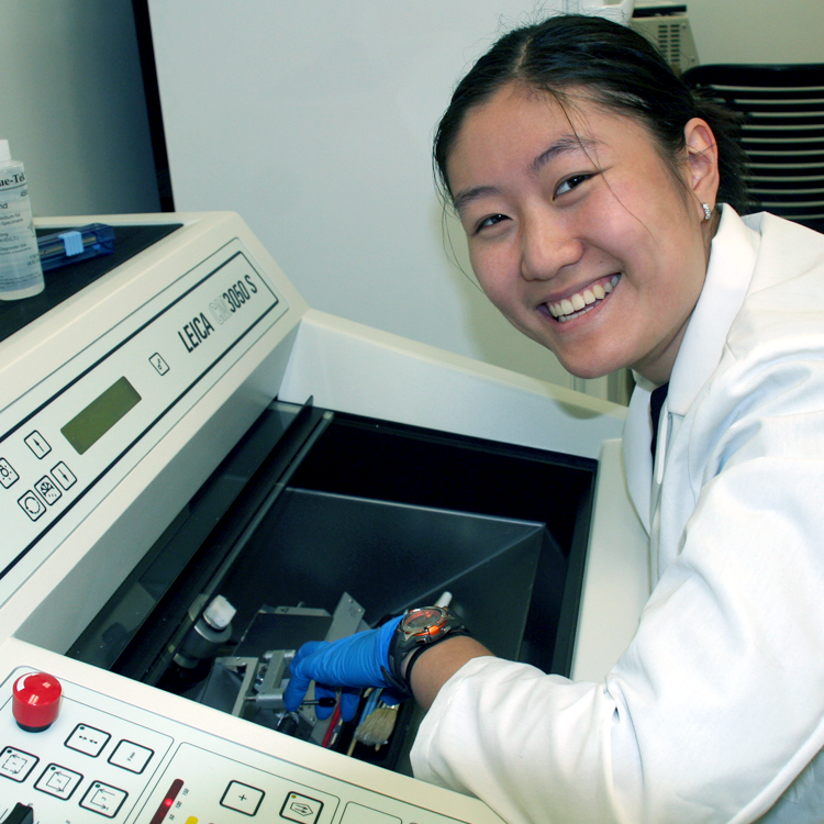 Photo of USRP student Scarlett Guo in the lab, putting samples into a large piece of equipment.