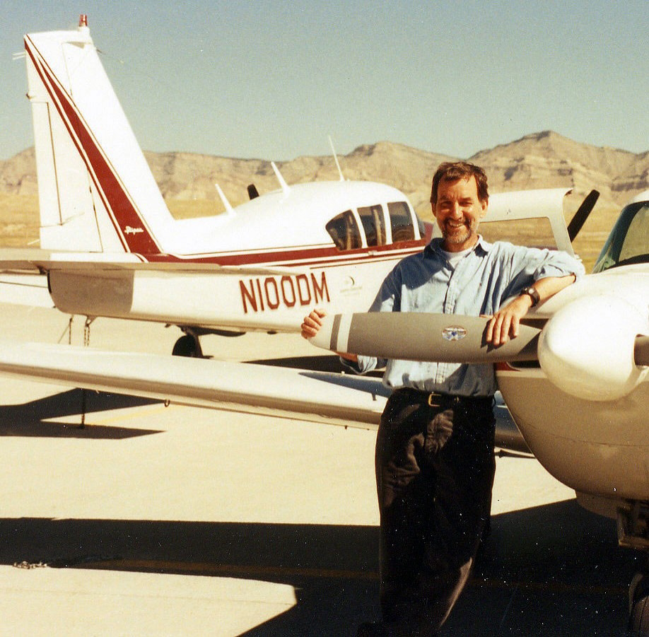 Photo of younger Dr. James Spudich standing outdoors in a desert area with two small private planes.