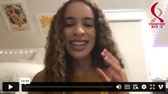 Screenshot of video showing a Black female undergraduate smiling indoors, gesturing with her hand.