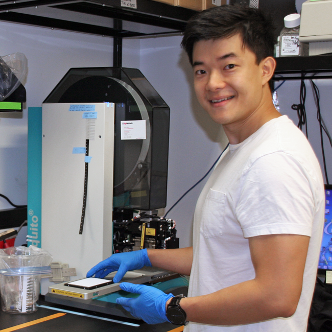 Photo of graduate student Yuan Xue in the lab, putting samples into a piece of equipment.
