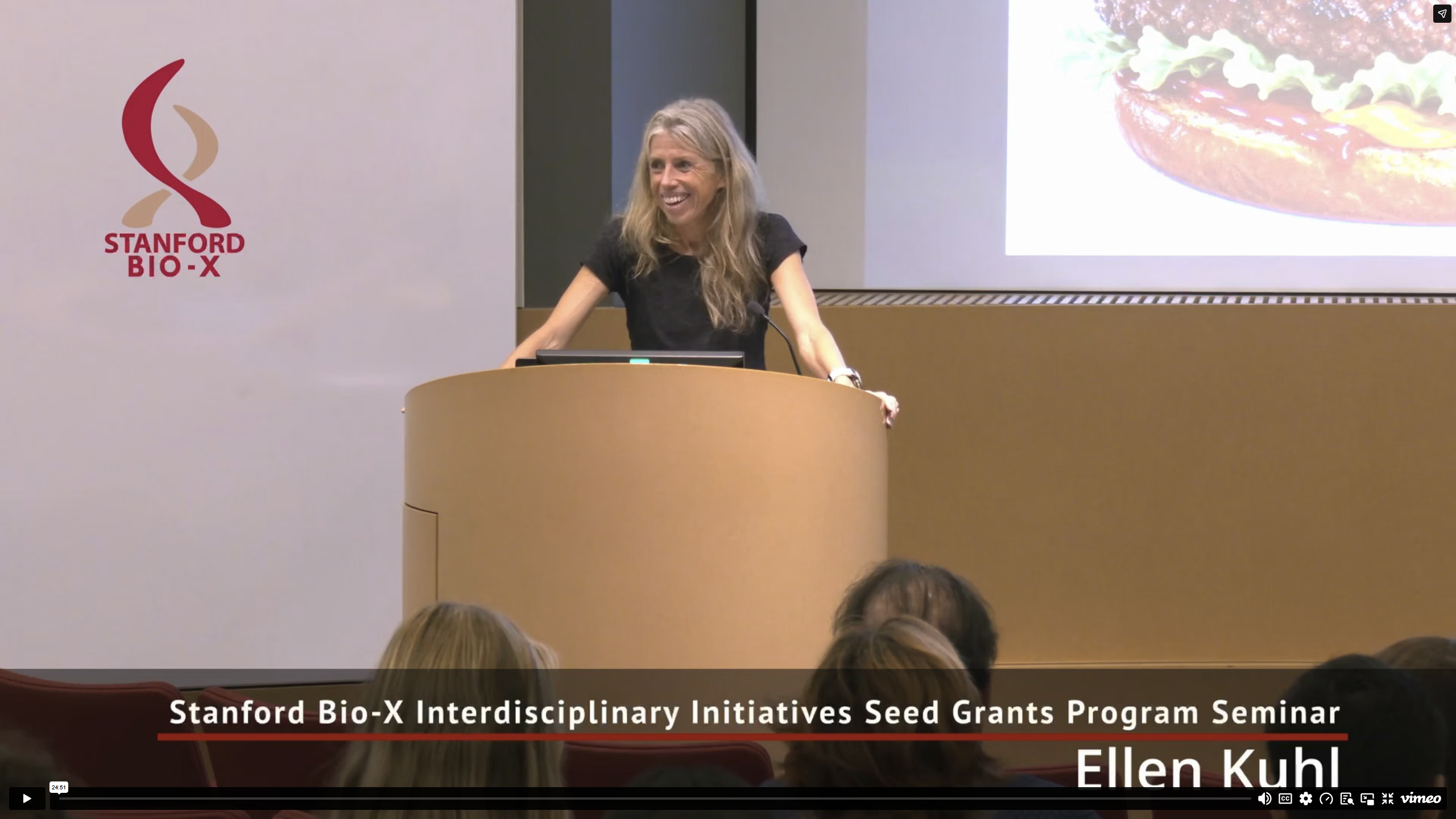 Video thumbnail showing faculty member standing at the front of an auditorium.