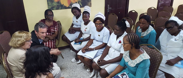 Photo of 3 Stanford faculty seated on left, having a discussion with several Nigerian nurses in uniforms.