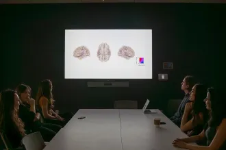Photo of a number of people sitting around a table in a dim conference room, with brain images displayed on the projector screen.