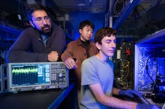 Interior laboratory photo of Stanford doctoral student Devin Dean preparing to measure an optical amplifier chip with Amir Safavi-Naeini and Taewon Park watching over his shoulder.