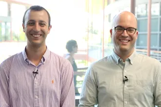 Indoor photo of Dr. Adam de la Zerda and Dr. Yonatan Winetraub, two adult white male faculty members at Stanford, standing side by side and smiling at the camera, one wearing glasses.