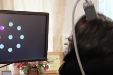 Screenshot from video showing paralyzed woman with device attached to head, using neural signals to manipulate cursor on a screen to select dots lighting up.