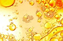 High-contrast photographic image of droplets on a flat surface, some coagulating with each other, in shades of yellow and orange.