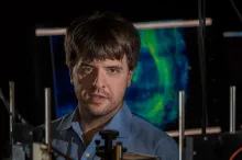 Photo of Dr. Karl Deisseroth in the laboatory, with colorful brain scans in the background.