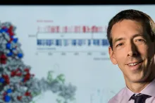 Photo of Dr. Euan Ashley in front of a screen showing a 3D image of a molecule.
